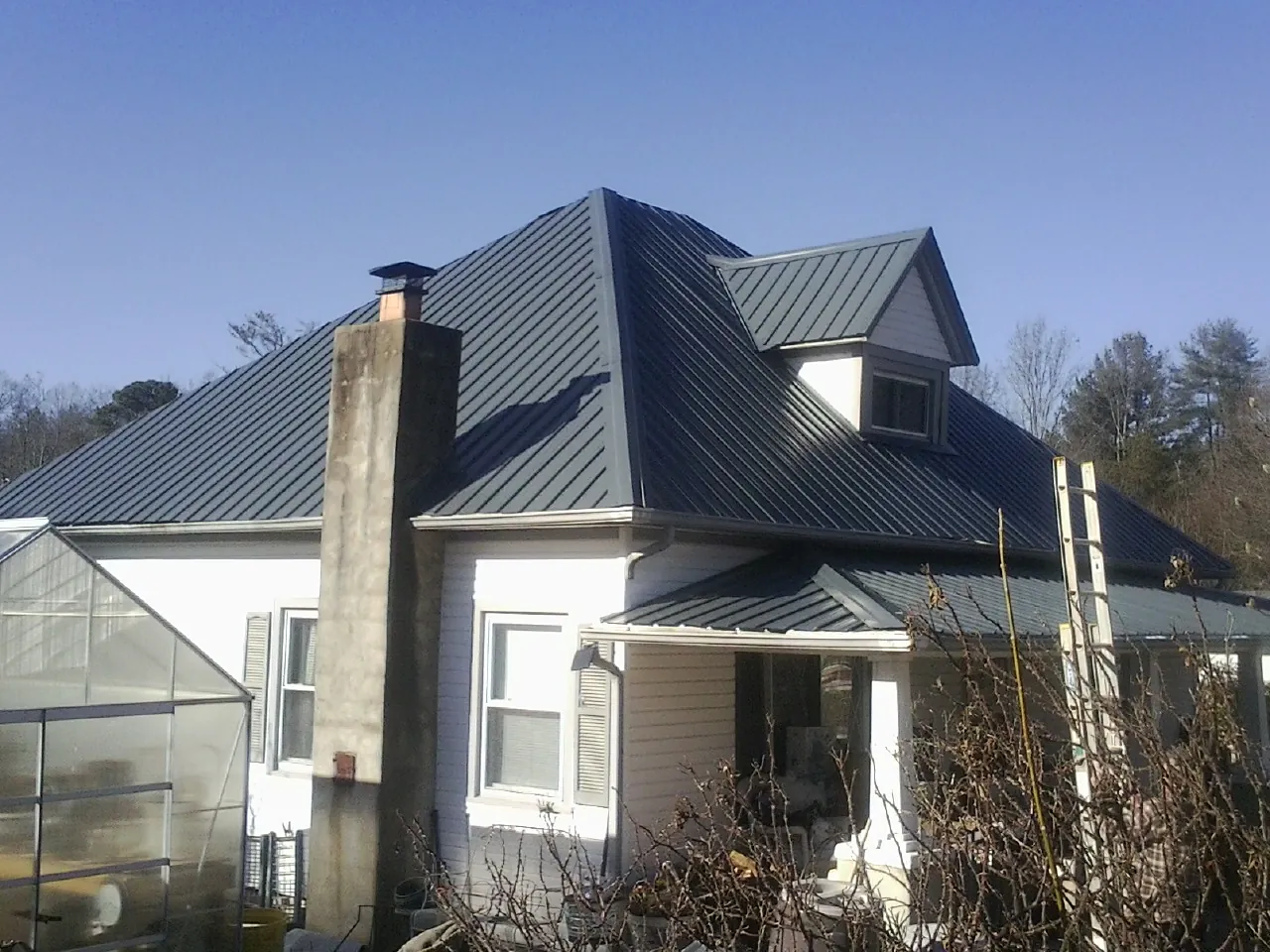 Dark blue standing seam metal roof on a white farmhouse with dormer — Slate & Tile Roof Repair by Roofing Brothers in Mc Connells