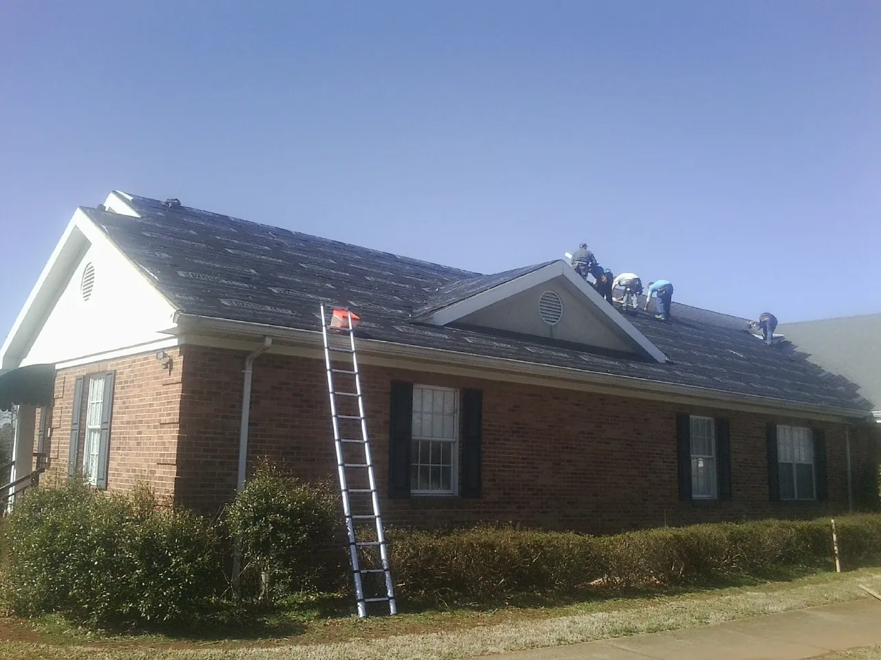 Crew tearing shingles off a brick ranch roof with a ladder set — Metal Roof Repair work by our crew in Mc Connells