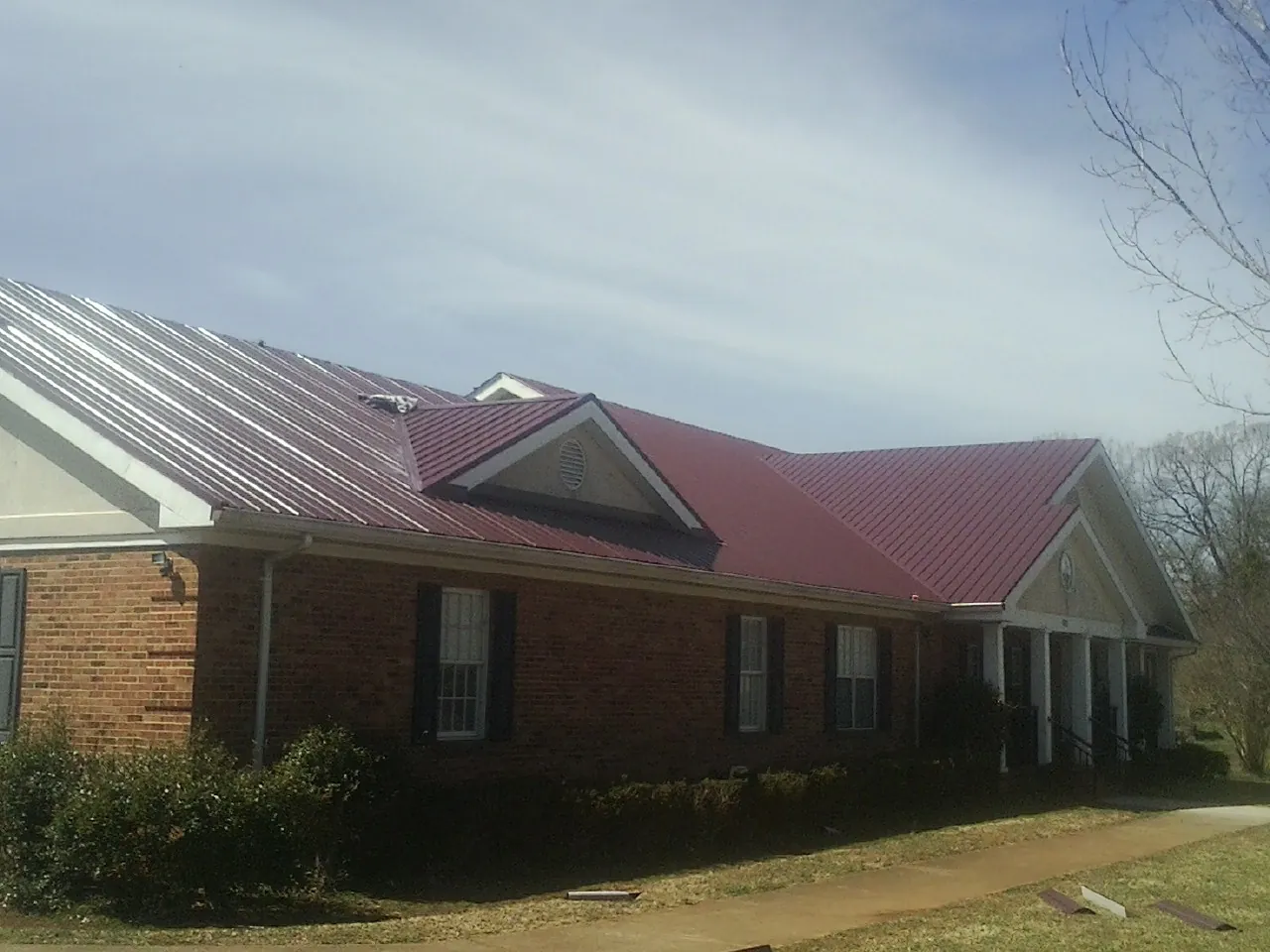 Red metal roof with gabled entries on a long brick building, from a Hail Damage Roof Repair job in Mc Connells