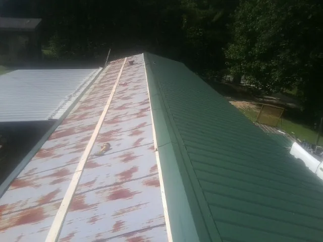Old rusted panels beside newly installed green metal roofing — Wind Damage Roof Repair by Roofing Brothers in Mc Connells