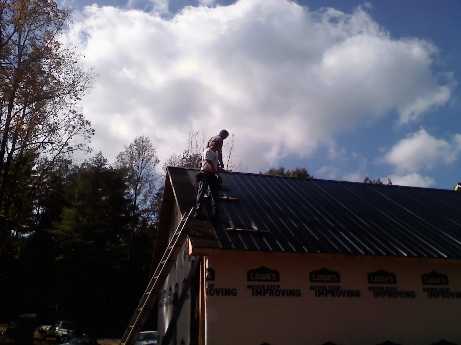 Roofer fastening dark metal panels high against a cloudy sky, from a Roof Inspection job in Mc Connells